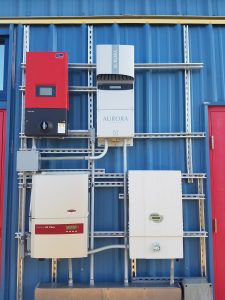 Four different inverters grouped together and mounted on blue, metal side of building, photo.