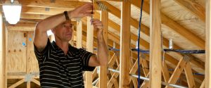 John Sherwin inspects a sensor in the attic of the Flexible Residential Test Structures, photo.