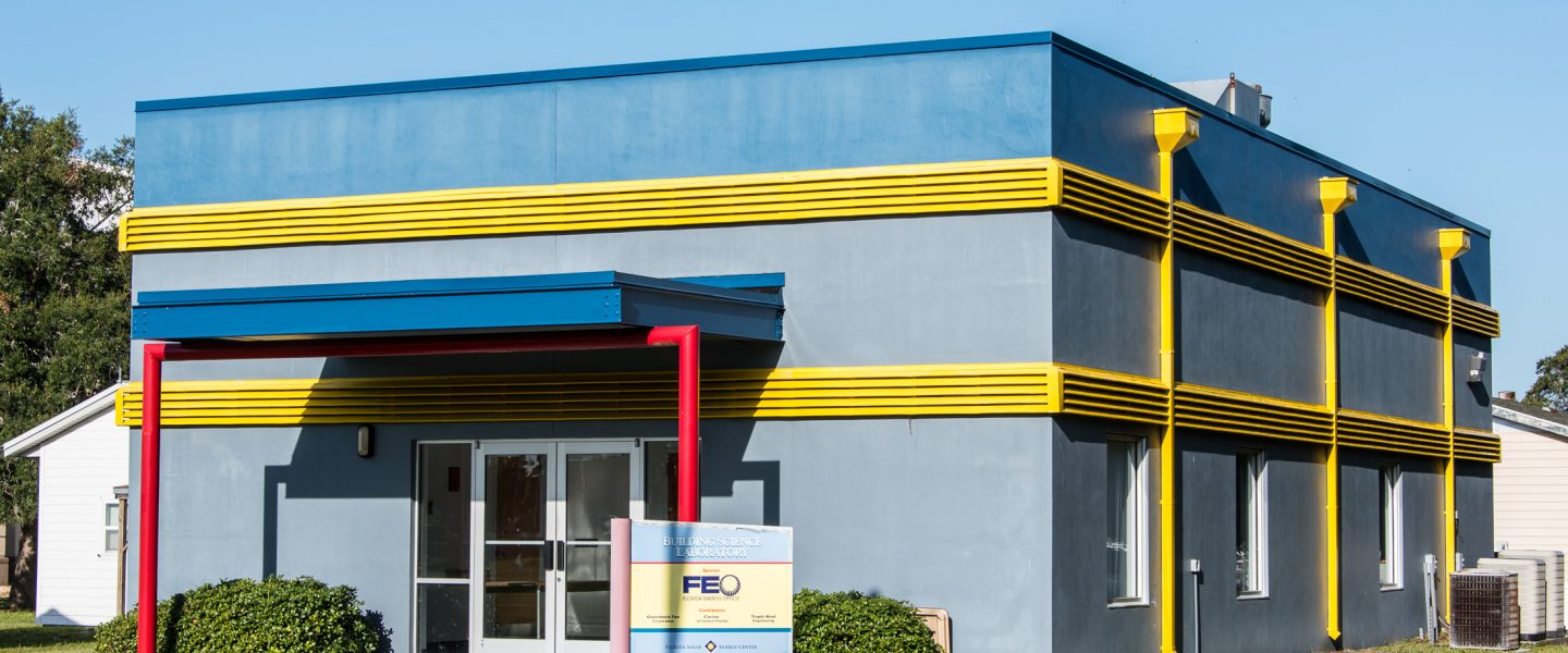 Small, one story commercial building painted in blue with yellow vents and red poles.