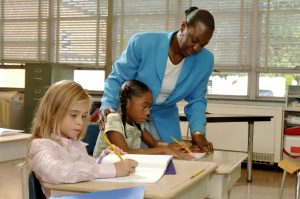 A teacher helps two young students in a classroom
