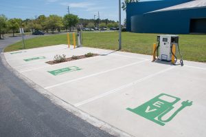 Electric vehicle public charging station–uncovered concrete pad with four parking spots–with Level 2 and Level 3 fast charger.
