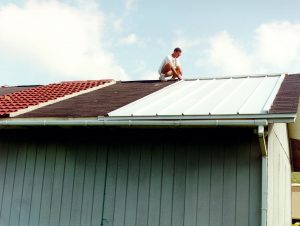 A 24 ft x 48 ft frame builidng with different roofing systems; man squatted down nest to white metal roof section; photo.