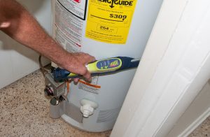 Student using a device to test for a gas leak near a gas powered water heater before a blower door test, weatherization