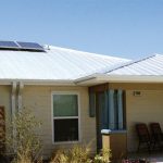 Duplex with light colored metal roof and solar electric panels on top, with large overhang on front for small, open porch.