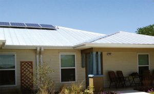 Duplex with light colored metal roof and solar electric panels on top, with large overhang on front for small, open porch.