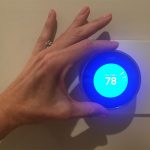 NEST smart thermostat being adjusted by female hand.