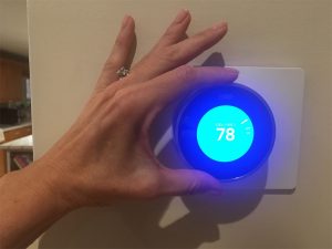 NEST smart thermostat being adjusted by female hand.