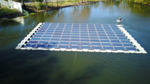 Floating photovoltaic system (10 panels x 10 panels) anchored in calm body of water, accessed by personal watercraft.