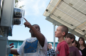 Two male students learn about solar energy by looking at an electric meter that is next to a solar electric array.